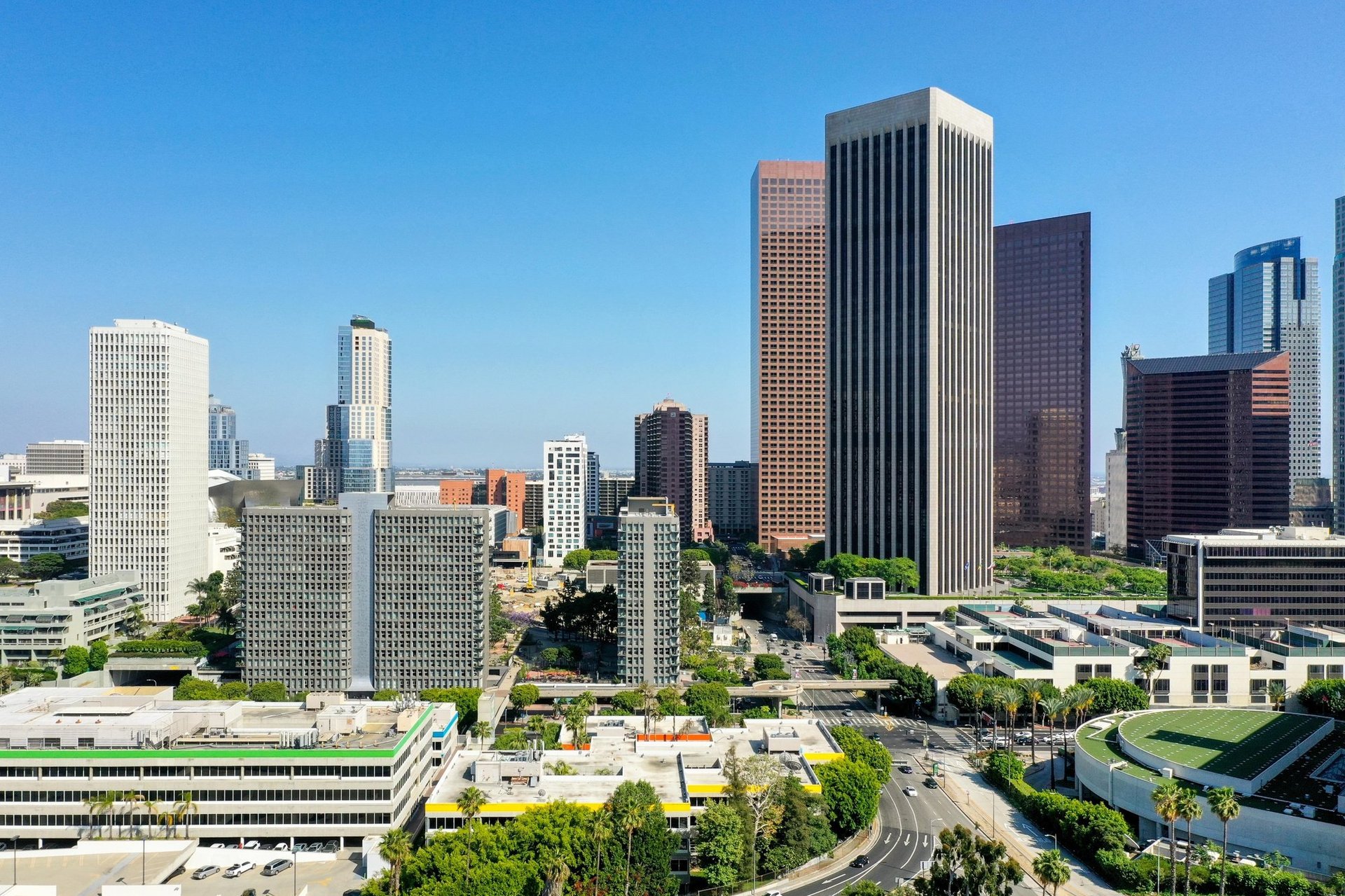 Aerial view of downtown cityscape with tall skyscrapers, green landscaping, and clear blue sky