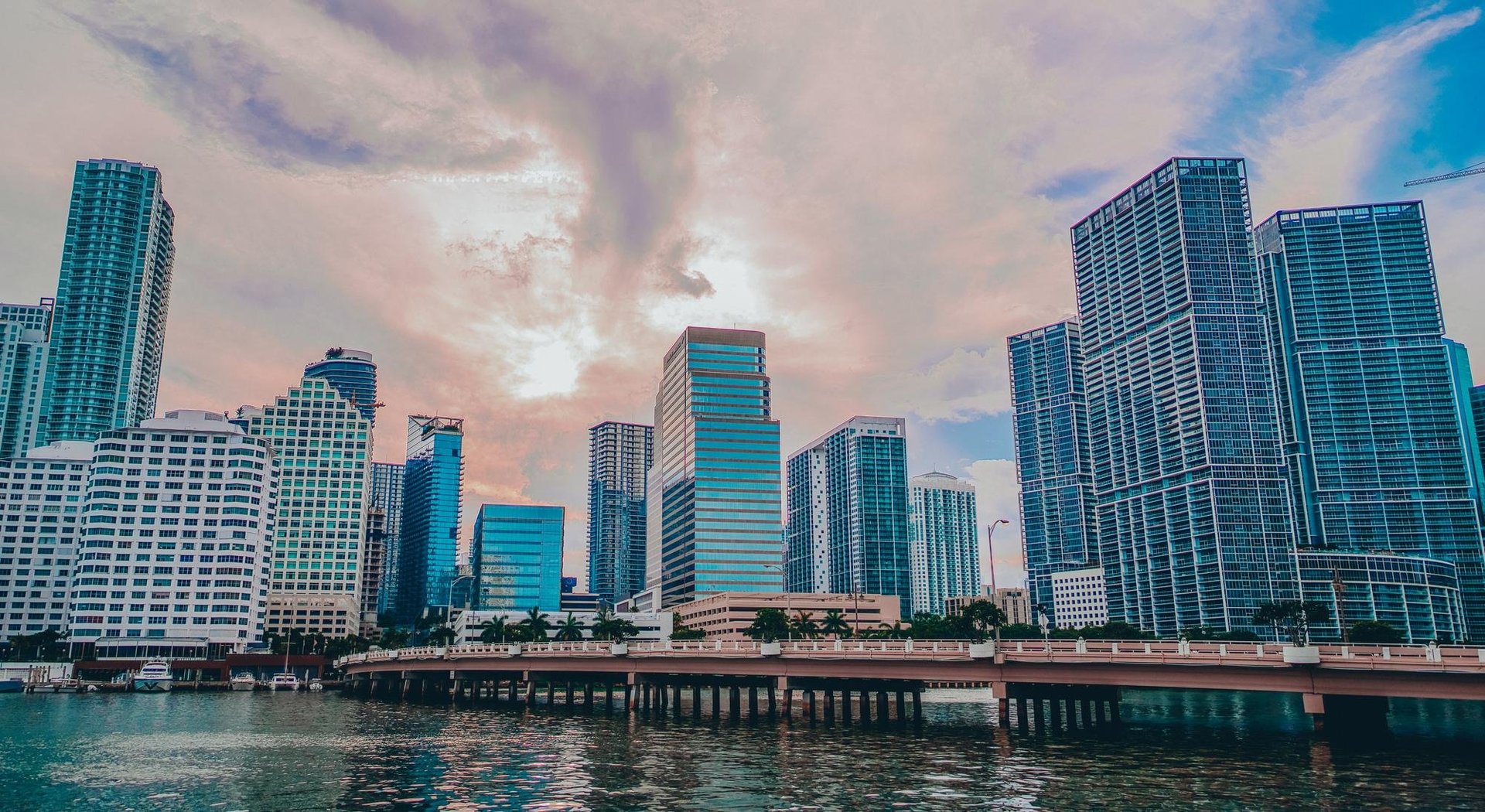Waterfront cityscape with modern high-rise skyscrapers, turquoise water, and dramatic clouds at dusk